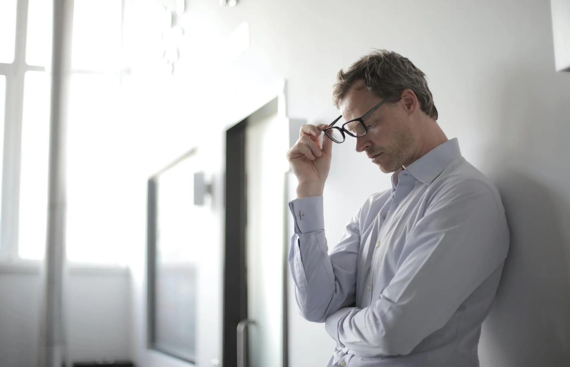 Man standing against a wall removing his glasses
