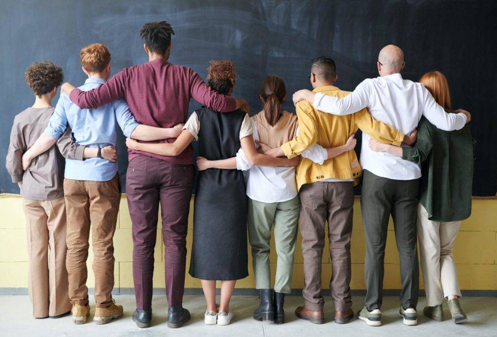 people standing together with arms wrapped around each other, facing away from camera