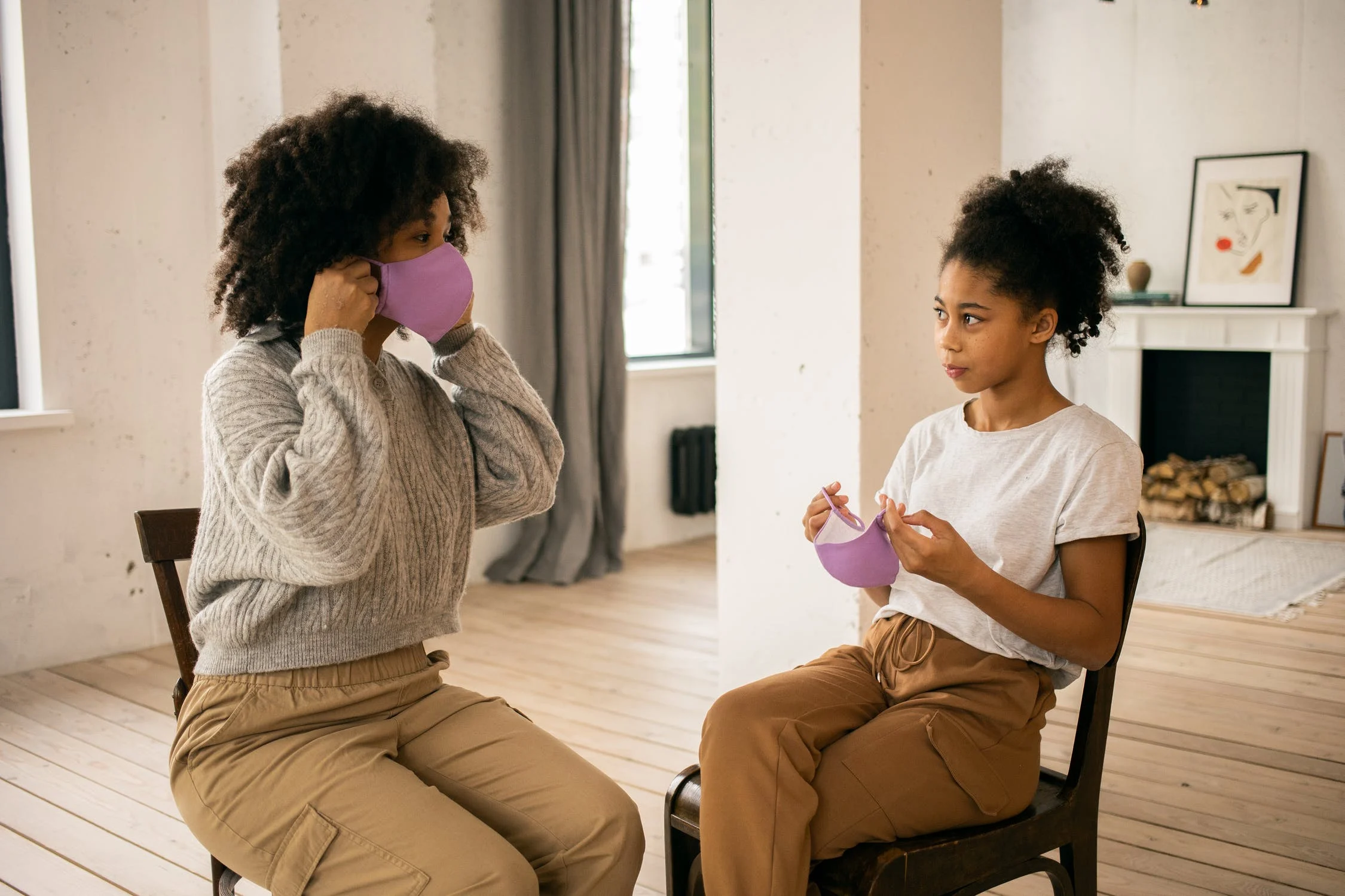 mother showing her daughter how to put on a face mask